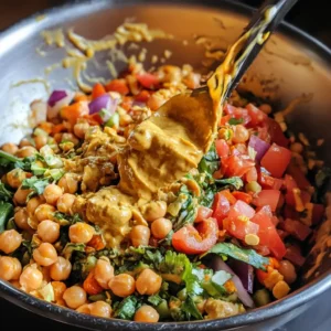 Curry peanut butter dressing being mixed into a chickpea salad with chopped vegetables in a large bowl